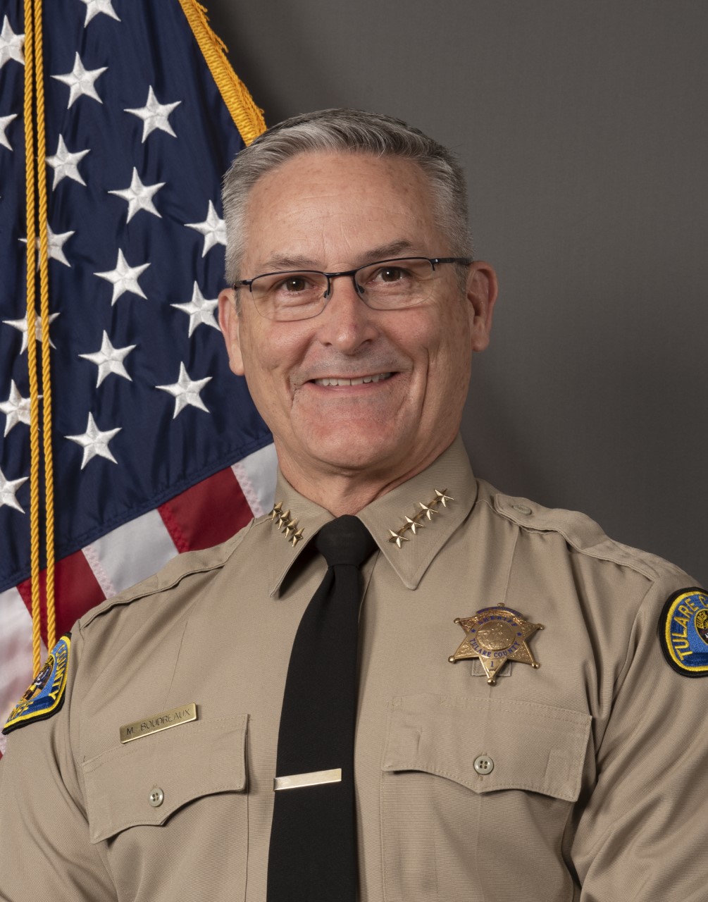 A head and shoulders portrait of Sheriff Mike Boudreaux with the American Flag pictured at left. 